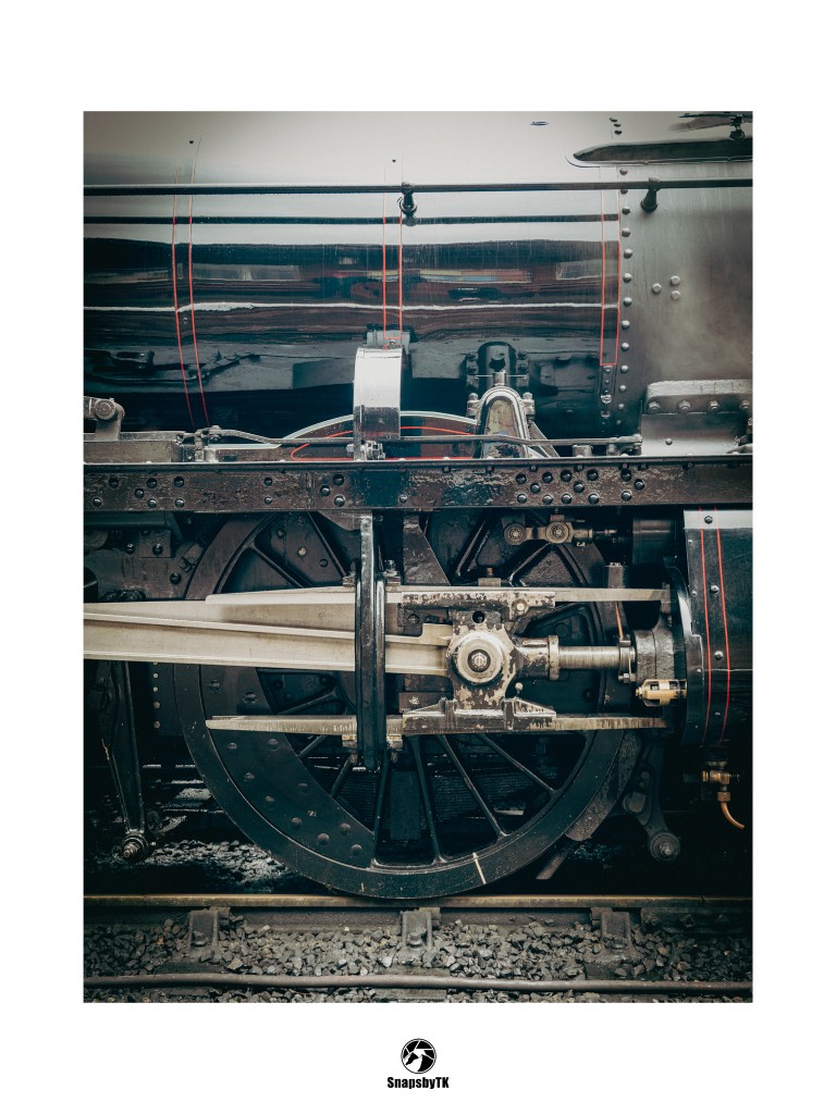 Close-up of a black vintage steam locomotive's large drive wheel and mechanical linkage. SnapsbyTK.
